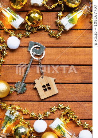 Key to house with a keychain tiny home on wooden background with Christmas decor layout. Gift for New Year, Christmas. Building, project, moving to new house, mortgage, rent and purchase real estate 109167707
