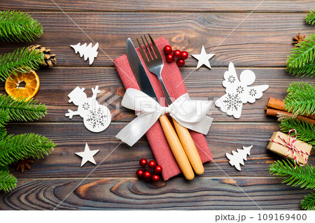Top view of utensils on festive napkin on wooden background. Christmas decorations with dried fruits and cinnamon. Close up of New year dinner concept Top view of utensils on festive napkin on wooden background. Christmas decorations with dried fruits and cinnamon. Close up of New year dinner concept 109169400