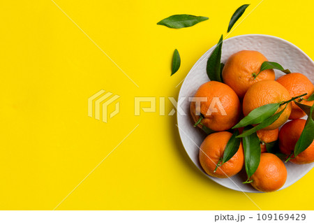 Fresh cutted clementines and whole mandarin over round plate on colored background. Food and drink ingredients preparing. healthy eating theme top view vith copy space Fresh cutted clementines and whole mandarin over round plate on colored background. Food and drink ingredients preparing. healthy eating theme top view vith copy space 109169429