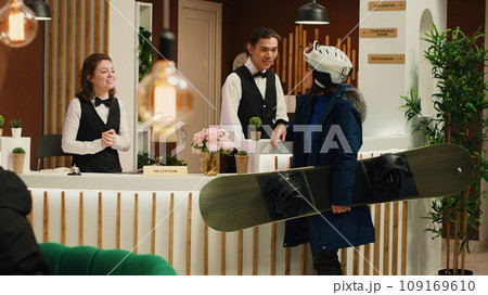 Woman asking staff about ski services, feeling impatient to start sliding down snowy slopes at mountain resort. Asian traveller talking to receptionist about snowboarding and winter sports. Woman asking staff about ski services, feeling impatient to start sliding down snowy slopes at mountain resort. Asian traveller talking to receptionist about snowboarding and winter sports. 109169610