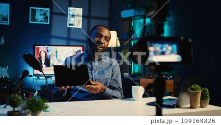 Content creator filming review of newly launched tablet, unboxing it and presenting specifications in apartment studio. Internet star showing digital device to fanbase, offering performance feedback 109169826