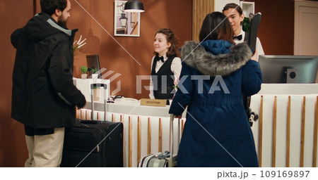 Hotel staff assisting couple at ski complex, travellers arriving for winter sport experiences on alpine slopes. Man and woman bringing mountain skiing gear for wintertime vacation. Handheld shot. 109169897