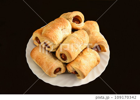 Many sausage rolls (pigs in a blanket) on white plate on black table Many sausage rolls (pigs in a blanket) on white plate on black table 109170342