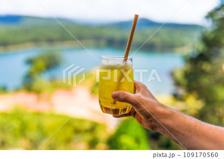 Glass of pineapple juice with ice in males hand against summer background 109170560