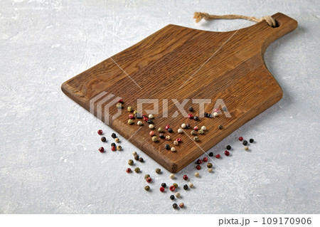 Brown wooden cutting board with scattered multi-colored peppercorns on a gray stone table Brown wooden cutting board with scattered multi-colored peppercorns on a gray stone table 109170906