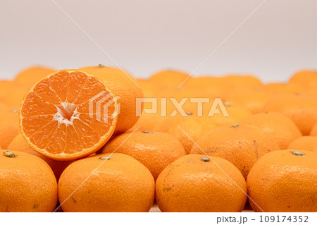 敷き詰められたミカンの上に、断面が見えている半分のミカンが乗っている 109174352