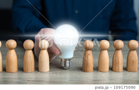 A man inserts a glowing light bulb idea between people. Inspire society to new ideas. Teamwork brainstorming. Research and development. Enlightenment and education. Ideology, paradigm A man inserts a glowing light bulb idea between people. Inspire society to new ideas. Teamwork brainstorming. Research and development. Enlightenment and education. Ideology, paradigm 109175090