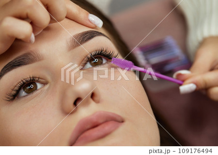 master combs the eyelashes of the client after the eyelash extension procedure. close-up. Cosmetology and skin care 109176494