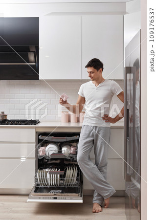 happy man taking out clean cup from dishwasher machine in the kitchen happy man taking out clean cup from dishwasher machine in the kitchen 109176537