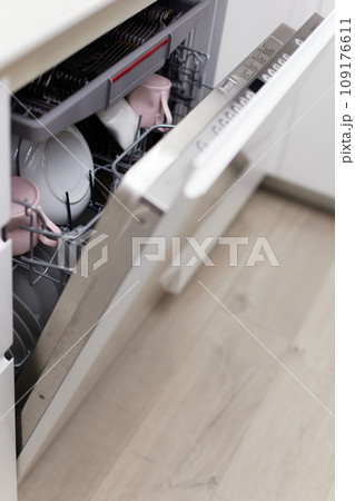 Open built-in dishwasher machine with clean cutlery, dishes, plates in white modern kitchen Open built-in dishwasher machine with clean cutlery, dishes, plates in white modern kitchen 109176611