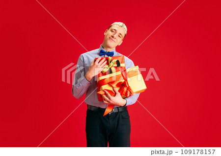 Portrait of happy smiling young am holding many presents against red studio background. Christmas, winter holidays 109178157