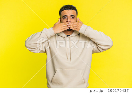 Frightened Indian man closing mouth with hands refusing to tell terrible secret, unbelievable truth 109179437
