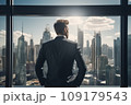 Young businessman standing in front of an office window, overlooking the city skyline 109179543