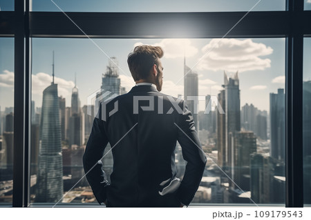 Young businessman standing in front of an office window, overlooking the city skyline 109179543