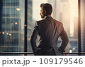 Young businessman standing in front of an office window, overlooking the city skyline 109179546