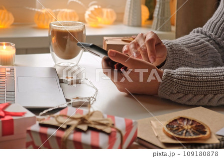 Woman using laptop and cell phone, making online purchases at cozy home. Holiday shopping. Gift present box, decoration. Winter sales, Black Friday. Christmas discount promotions. Blurred bokeh light Woman using laptop and cell phone, making online purchases at cozy home. Holiday shopping. Gift present box, decoration. Winter sales, Black Friday. Christmas discount promotions. Blurred bokeh light 109180878