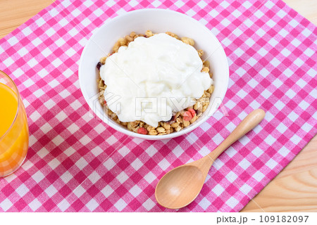 ランチョンマット上の白い皿に入ったシリアルとヨーグルト　フルーツグラノーラ　朝食　健康食品 109182097