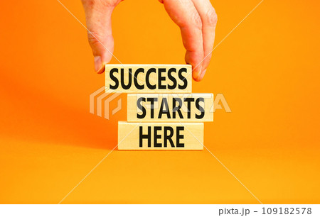 Success starts here symbol. Concept word Success starts here on beautiful wooden block. Businessman hand. Beautiful orange background. Business motivational success starts here concept. Copy space. 109182578