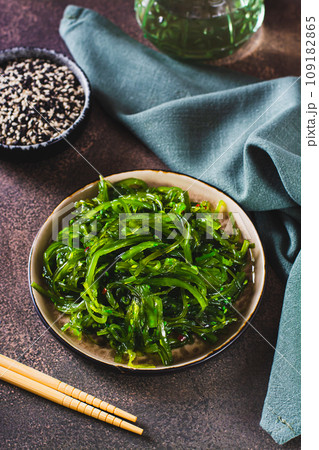 Delicious wakame seaweed salad on a plate and sesame seeds in a bowl on the table vertical view Delicious wakame seaweed salad on a plate and sesame seeds in a bowl on the table vertical view 109182865