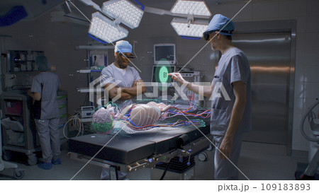 Diverse male surgeons in AR headsets work in operating room 109183893