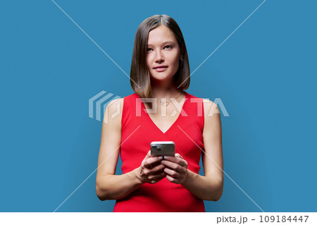 Young woman with smartphone in hands on blue studio background 109184447