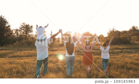 Strong friendly family with children walks raising hands across meadow at sunset 109185963