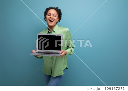 young brunette hispanic woman with curly hair in green rejoices holding a laptop in her hand against young brunette hispanic woman with curly hair in green rejoices holding a laptop in her hand against 109187271