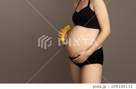 Pregnant woman stand in room and holding banana at Pregnant woman stand in room and holding banana at 109188132
