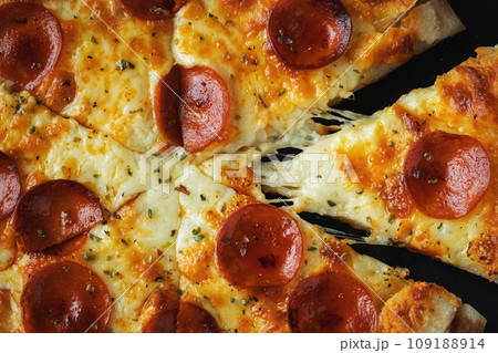 A slice of hot Italian pizza with stretching cheese. Pizza pepperoni on a dark wooden background A slice of hot Italian pizza with stretching cheese. Pizza pepperoni on a dark wooden background 109188914