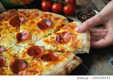 A slice of hot Italian pizza with stretching cheese. Pizza pepperoni on a dark wooden background 109188933