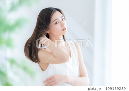 リビングの窓際でヘアケアをする若い女性 リビングの窓際でヘアケアをする若い女性 109189289