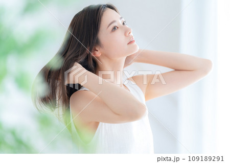 リビングの窓際でヘアケアをする若い女性 109189291