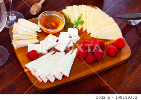 Cheese platter on wooden board with raspberries and honey Cheese platter on wooden board with raspberries and honey 109189352
