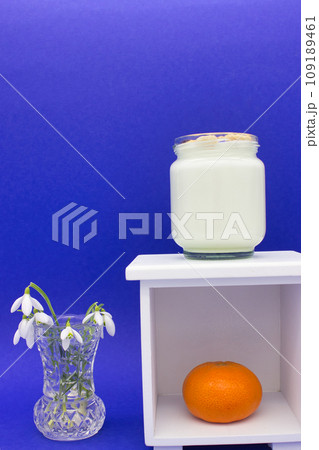 A glass jar of yogurt and an orange on a white shelf 109189461
