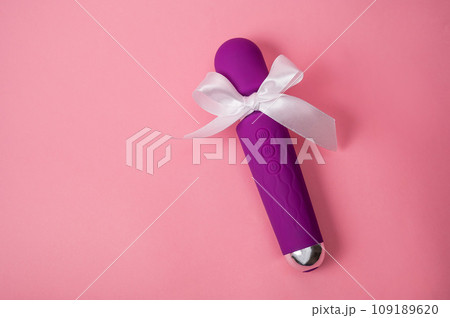 Purple vibrator with a white bow on a pink background. Women's gift. Purple vibrator with a white bow on a pink background. Women's gift. 109189620