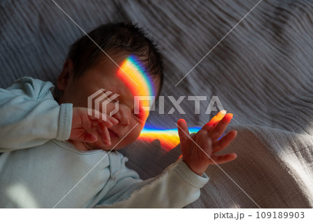Close-up portrait of a newborn boy with a prism beam on his face. Rainbow. Close-up portrait of a newborn boy with a prism beam on his face. Rainbow. 109189903