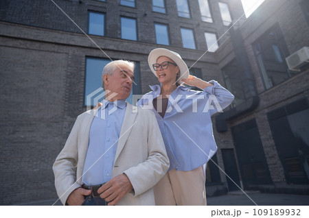 A woman in a hat and glasses hugs an elderly man in a white jacket from behind. Romantic relationships of mature people. A woman in a hat and glasses hugs an elderly man in a white jacket from behind. Romantic relationships of mature people. 109189932