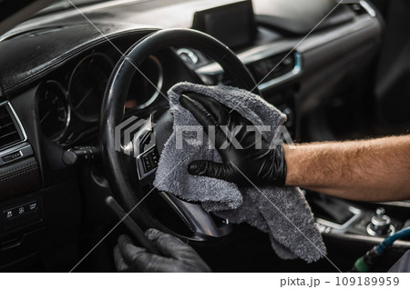 A mechanic wipes the steering wheel of a car with a microfiber cloth. A mechanic wipes the steering wheel of a car with a microfiber cloth. 109189959