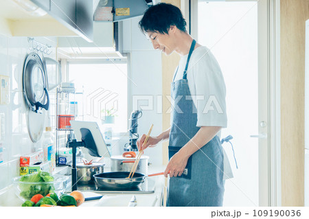 タブレットを見ながら料理をする男性 109190036