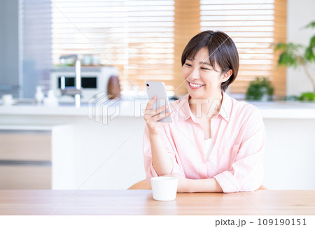 リビングでコーヒーを飲みながらスマホを使う女性。 リビングでコーヒーを飲みながらスマホを使う女性。 109190151