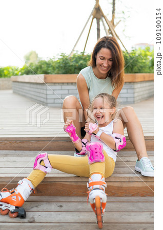 Little girl in roller skates and her mom sit on a wooden ladder and hug outdoors.  109190154