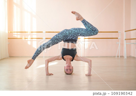 Flexible Caucasian girl stands on her head in a dance class. The girl does yoga. . Woman dancing breakdance on the background of ballet barre. Flexible Caucasian girl stands on her head in a dance class. The girl does yoga. . Woman dancing breakdance on the background of ballet barre. 109190342