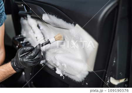A man cleans the interior of a car with foam and a brush. Clean the door trim. A man cleans the interior of a car with foam and a brush. Clean the door trim. 109190376