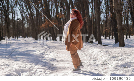 Portrait of an excited red-haired curly fat woman in the park in winter. Portrait of an excited red-haired curly fat woman in the park in winter. 109190459