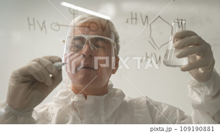 An elderly Caucasian male chemist in a protective suit writes on glass.  109190881