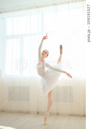 Beautiful ballerina in body and white tutu is training in a dance class. Young flexible dancer posing in pointe shoes. Beautiful ballerina in body and white tutu is training in a dance class. Young flexible dancer posing in pointe shoes. 109191027