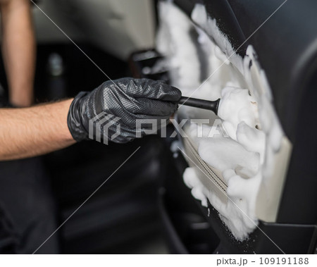 A man cleans the interior of a car with foam and a brush. Clean the door trim. 109191188