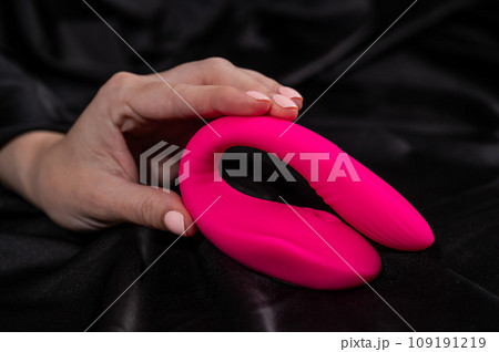 A woman holds a pink curved vibrator while lying on a black silk sheet. A woman holds a pink curved vibrator while lying on a black silk sheet. 109191219