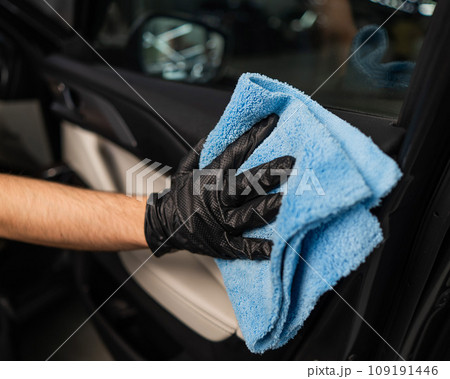 A man wipes the surface of the car interior with a microfiber cloth. A man wipes the surface of the car interior with a microfiber cloth. 109191446