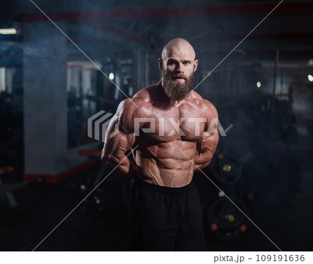 Muscular bald man posing shirtless. Bodybuilder showing off his shape in the gym. Muscular bald man posing shirtless. Bodybuilder showing off his shape in the gym. 109191636